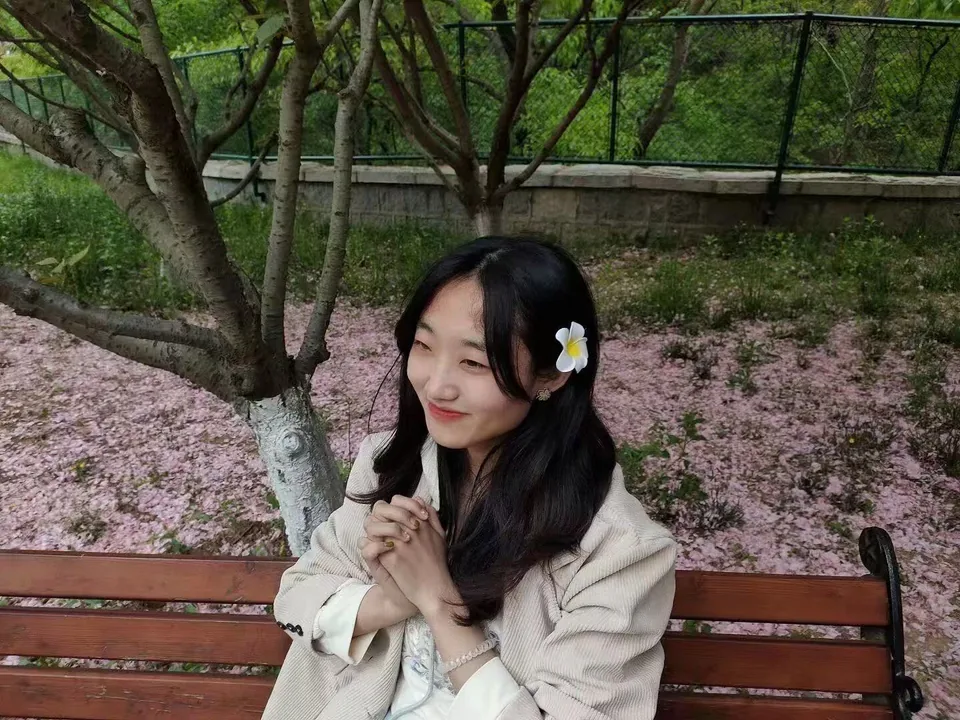 女性坐在花树下的长椅上，周围有落花