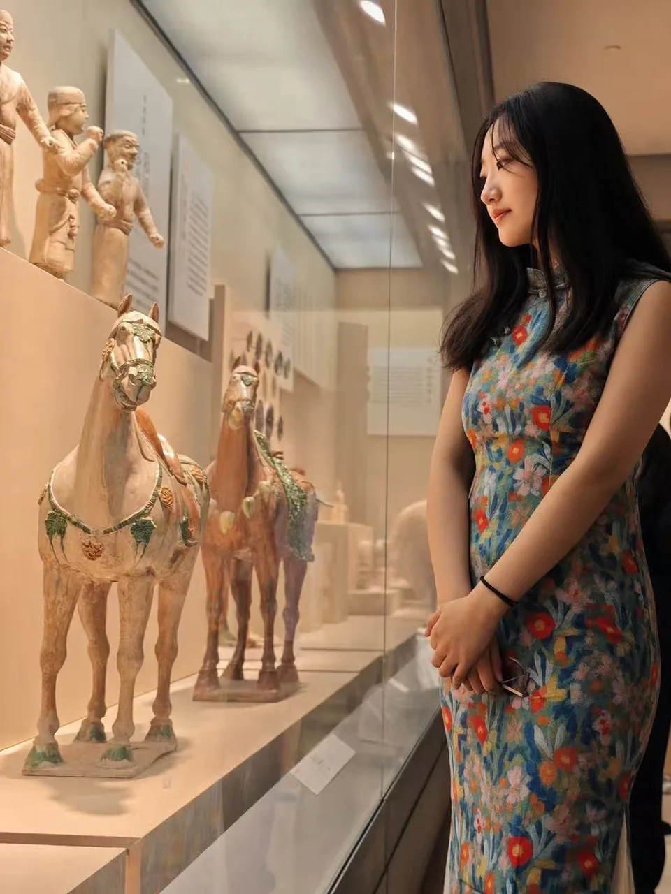 女性站在暖色展柜前，旁边陈列着陶塑展品
